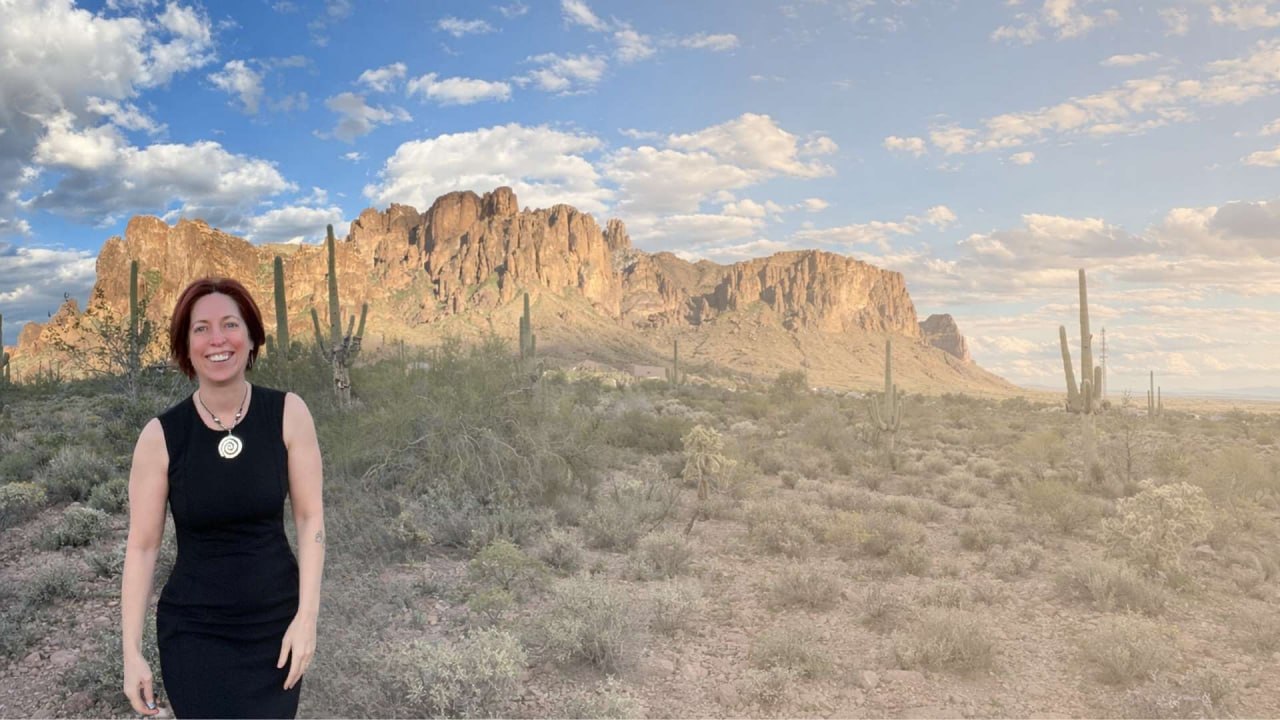 Kirstin standing in an open desert landscape with mountains, sky, and saguaro cactus behind her.